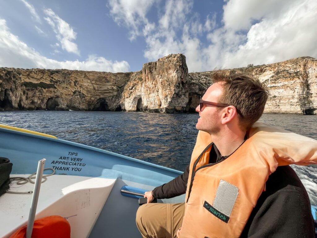 Matthias sitting in a boat with a life vest and in the background the cliffs of Malta