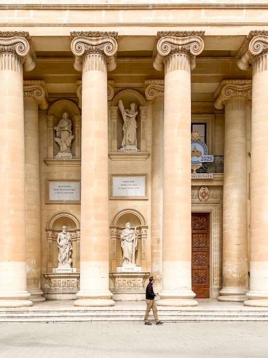 Matthias walking in front of the Mosta Rotunda, indicating how big this church is compared to himself