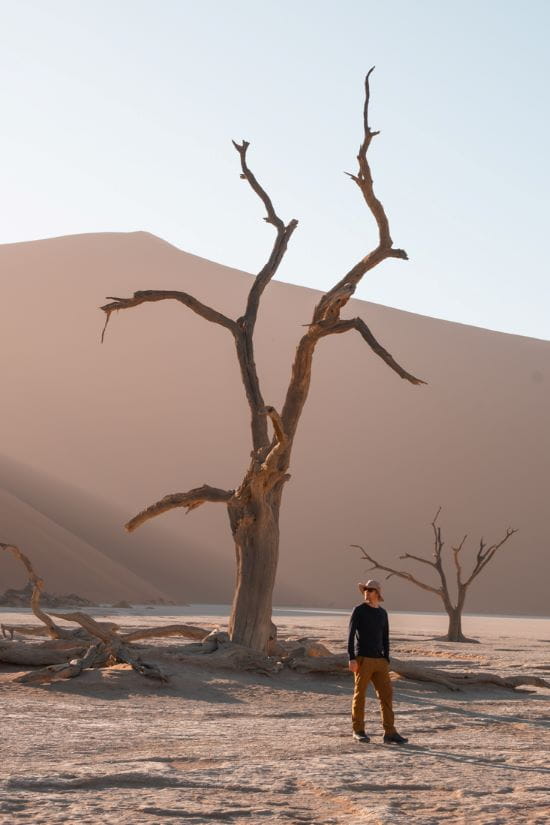 Matthias stands beside a tall, skeletal dead tree on the white clay floor of Deadvlei, Namibia.