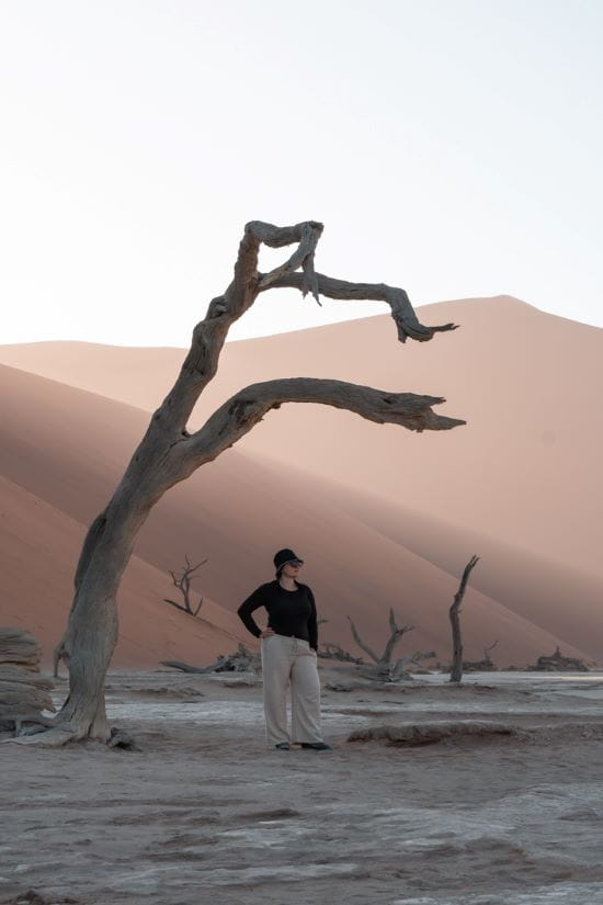 Mieke standing beneath the dramatic arching branch of a dead tree in Deadvlei, Namibia.