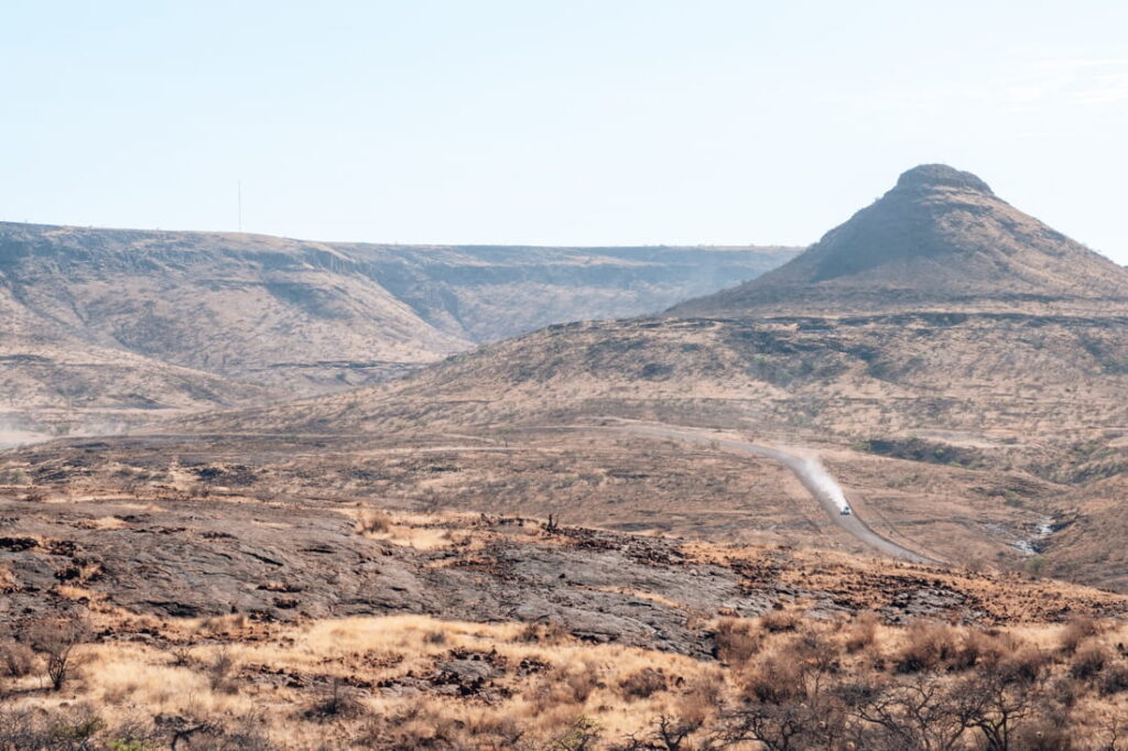 A white 4x4 car drives along a winding dirt road through the arid, rocky mountains of Grootberg Pass.
