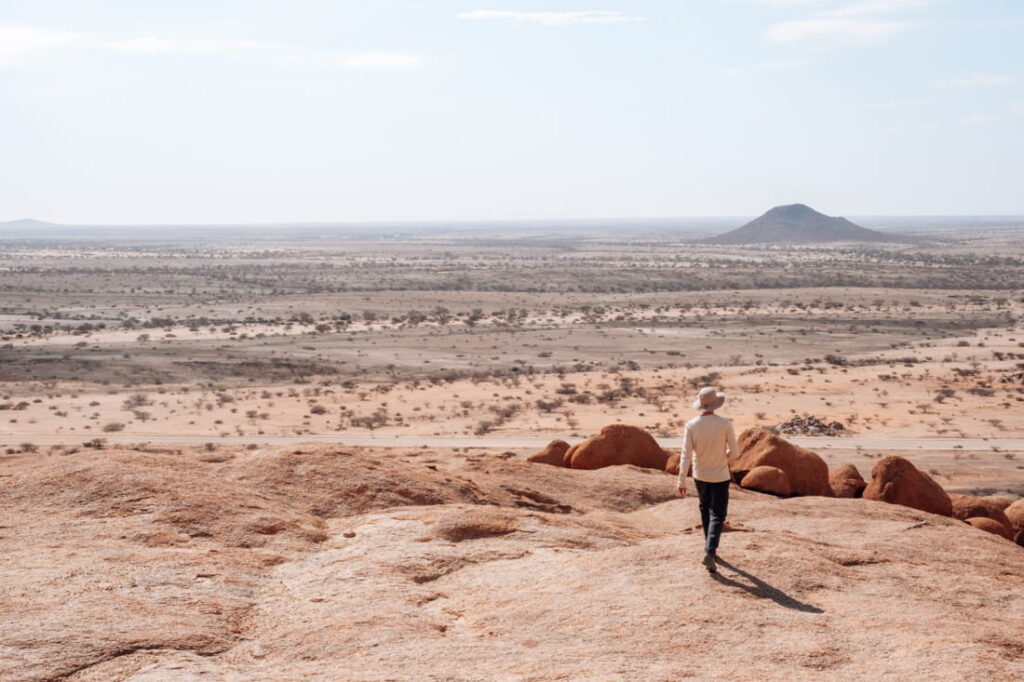 Matthias walking down a smooth granite mountain ridge looking out over a wide flat plain.