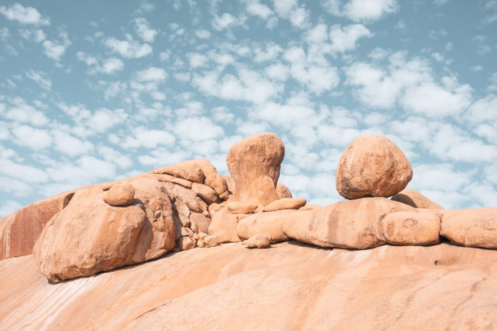 Large, rounded orange granite boulders are stacked under a cloudy blue sky.