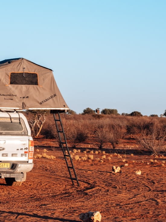 Witte 4x4 pick-up met uitgeklapte daktent in het rode woestijnzand van de Kalahari.