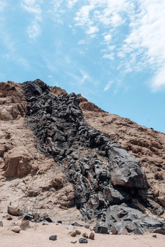 Dark volcanic dolerite rock ridge cutting through a lighter granite hillside in the Namib Desert.