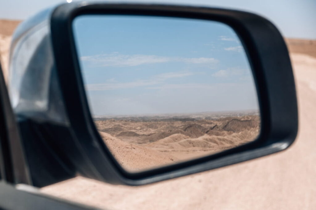 Car side mirror reflecting the desert canyons of the Moon Landscape under a blue sky in Namibia.