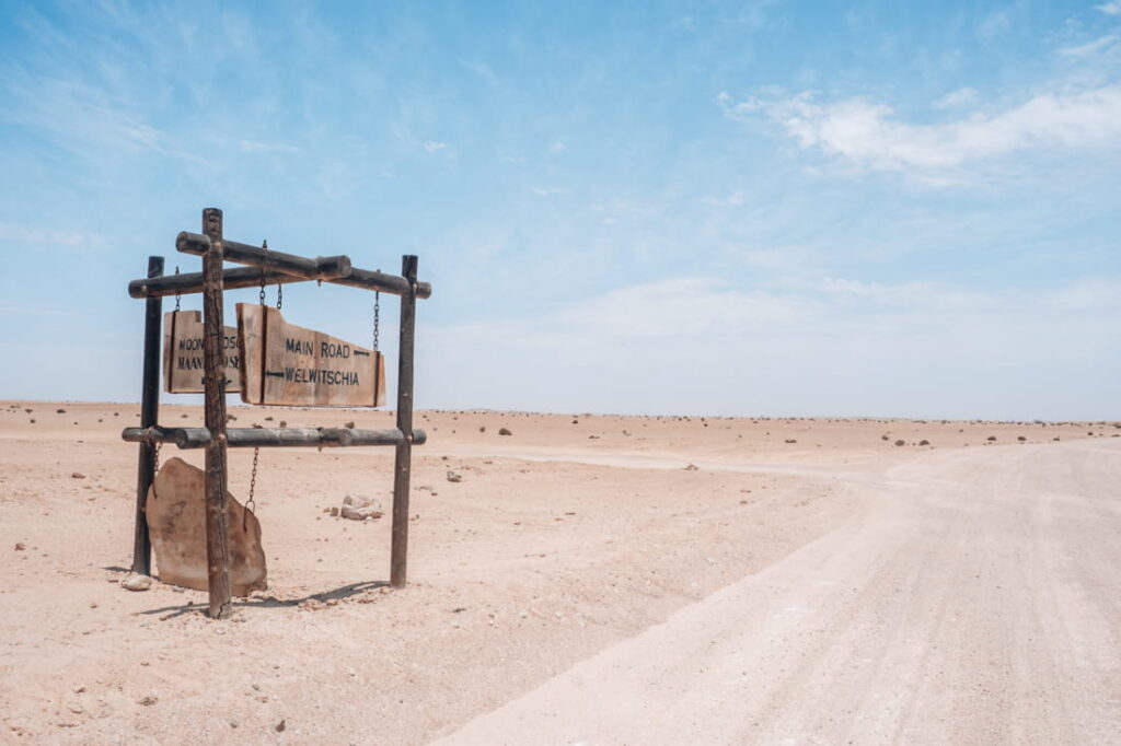 Wooden directional sign post of the Welwitschia drive standing on a gravel desert road turnoff in the Namib Desert, Namibia.